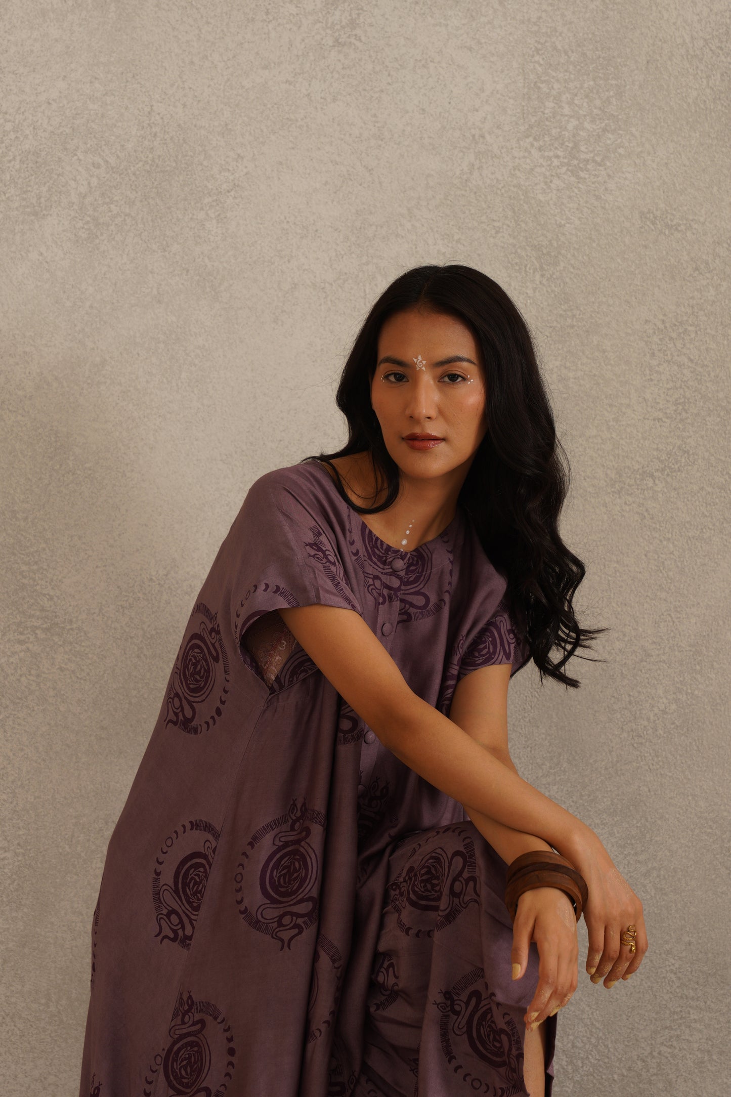 Woman wearing a purple patterned dress against a beige background